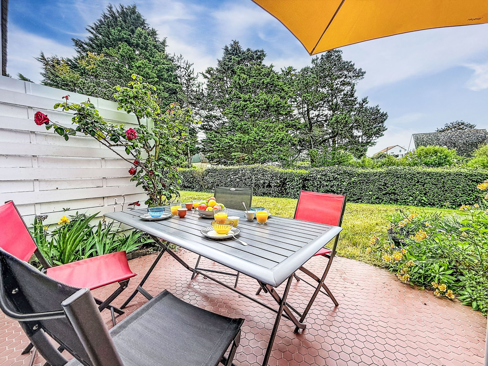 An outdoor patio with a table, chairs, and a yellow umbrella.