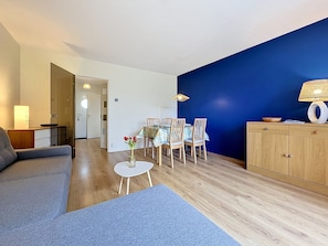 Ein modernes Wohnzimmer mit einer Couch, einem Esstisch mit Stühlen, einem kleinen Beistelltisch mit einer Vase und einem Schrank.