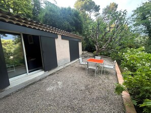 A building with a tiled roof, a sliding glass door, and a gravel patio with a table and chairs.