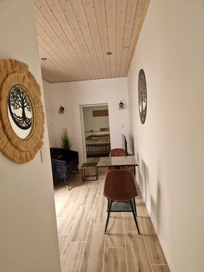 A room with a wooden ceiling, a dining table with chairs, a sofa, and a decorative wall piece. - Maisonnette avec terrasse (Saint-Gilles-Croix-de-Vie)