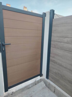 Een gesloten houten poort met een zwarte omlijsting, voor een gebouw met een grijze gevel.