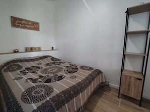 A bedroom with a bed, a shelf with decorative items, and a wooden cabinet. - Maisonnette avec terrasse (Saint-Gilles-Croix-de-Vie)