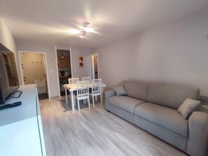 A living room with a sofa, a dining table with chairs, and a ceiling fan. - Proche commerces vue foret (Saint-Jean-de-Monts)