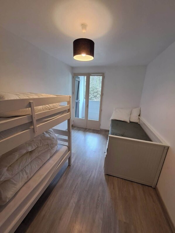 Una habitació petita i ben il·luminada amb una llitera, un escriptori i una finestra.