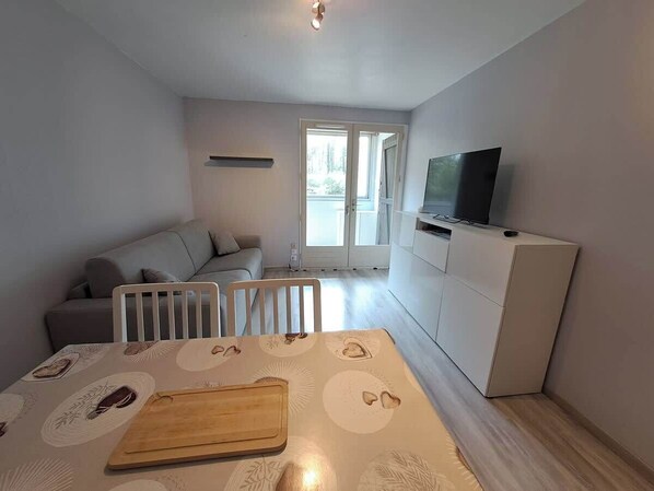 A compact living space with a dining area, a sofa, a TV, and a kitchenette. - Proche commerces vue foret (Saint-Jean-de-Monts)