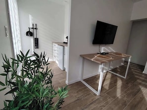 Un salon moderne avec un téléviseur fixé au mur, une table à manger en bois et une plante en pot.