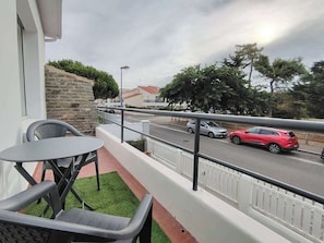Un balcon avec une table et des chaises, un mur en pierre et une vue sur une route où circulent des voitures.