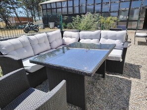 Un espace extérieur aménagé avec une table à plateau de verre et des chaises rembourrées, le tout entouré de gravier.