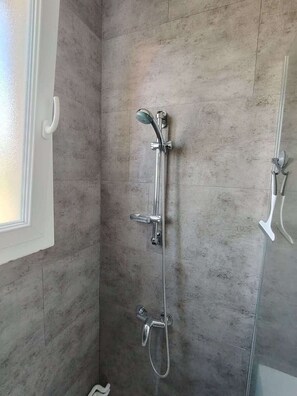 Un espace douche doté d’une porte en verre, d’un pommeau de douche à main et d’un robinet mural.