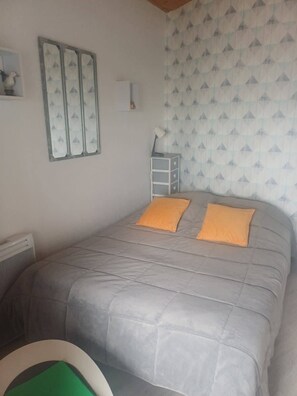 Une chambre à coucher avec un lit, deux oreillers, une table de chevet, une lampe et une étagÚre fixée au mur.