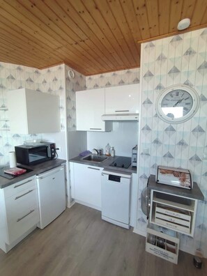 Una cocina compacta con armarios blancos, un microondas, un fregadero y un reloj en la pared.