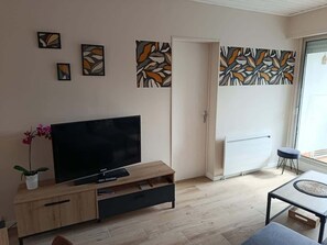 Una sala de estar con televisor sobre un mueble de madera, una mesita pequeña y arte abstracto en la pared.