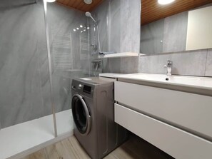Un baño moderno con lavadora integrada, cabina de ducha y tocador con espejo.