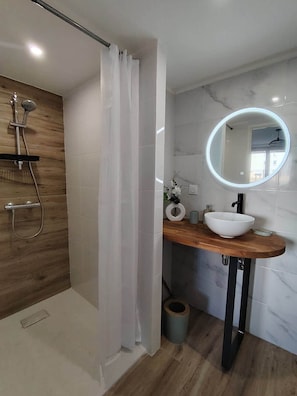 Un bagno moderno con box doccia in legno, lavabo bianco su piano in marmo e specchio rotondo con illuminazione a LED.
