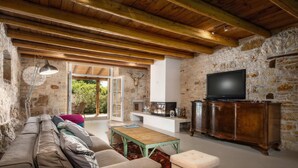 A rustic living room with a stone wall, wooden beams, a sofa, a coffee table, a television, and a cabinet. - Villa Eva Rustica (100591-K1) - Zbandaj (Zbandaj)