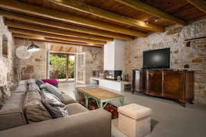 Ein rustikales Wohnzimmer mit Steinwand, Holzbalken, einer Couch, einem Couchtisch, einem Fernseher und einem Schrank.