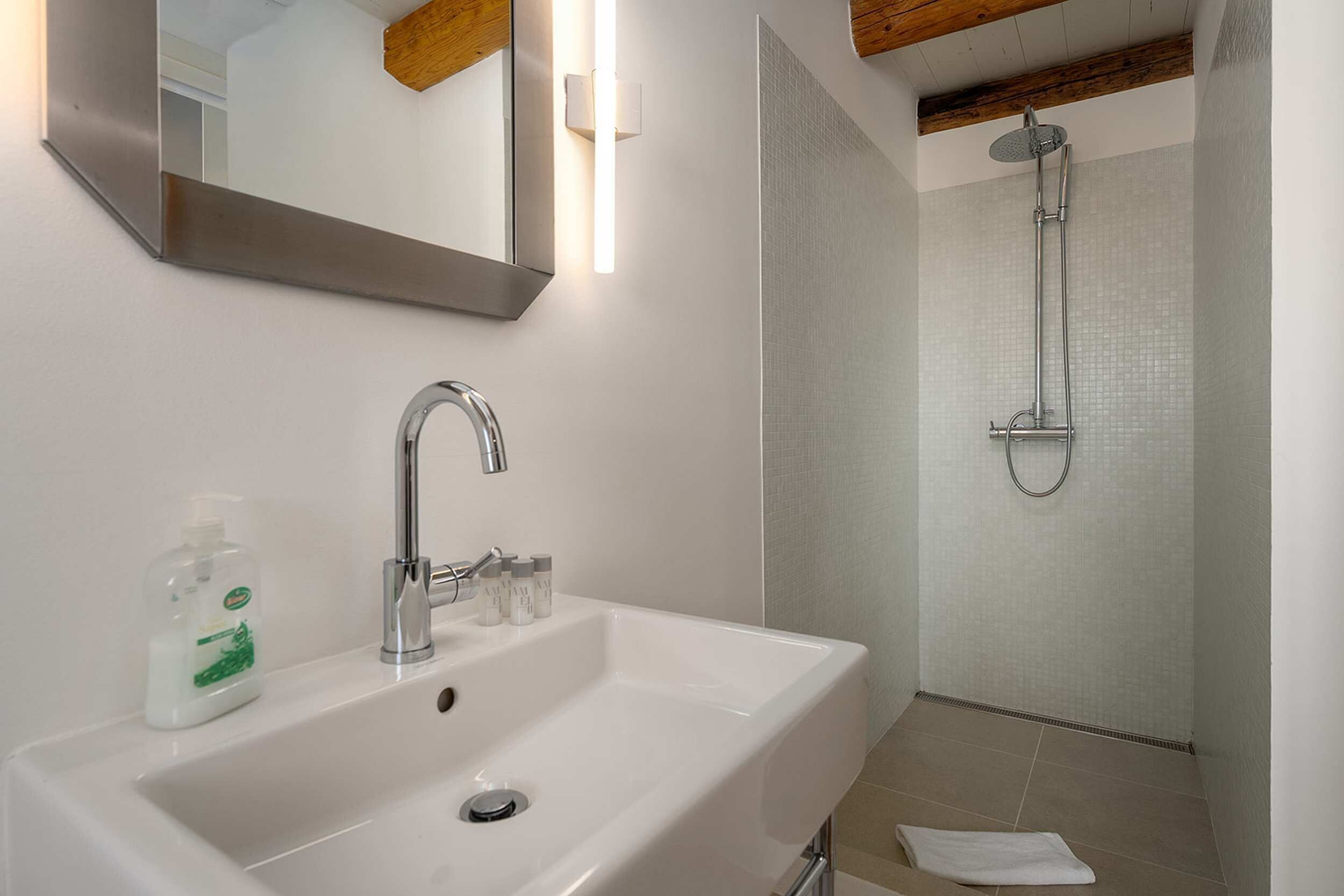Une salle de bain avec un lavabo blanc, un miroir, une douchette à main et une serviette sur le sol.