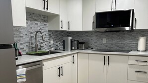 Eine moderne Küche mit weißen Schränken, einem Edelstahlkühlschrank, einer Mikrowelle und einer Kaffeemaschine.
