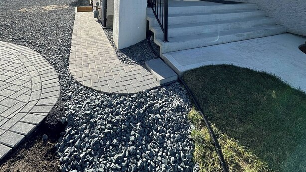 Ein modernes Haus mit überdachter Veranda, Stufen zum Eingang und einem Schotterweg.