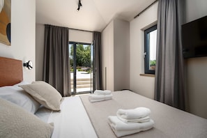 Ein Hotelzimmer mit Bett, Fernseher, Fenster mit Vorhängen und Blick ins Freie.