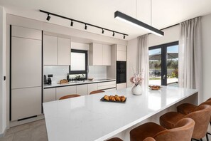 Eine moderne Küche mit weißen Schränken, einer großen Kochinsel mit Sitzgelegenheiten und Blick ins Freie.
