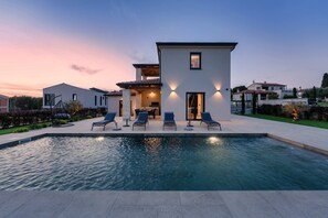 Et moderne hus med swimmingpool, udendørs møbler og en velplejet have.
