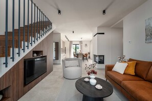 Ein modernes Wohnzimmer mit Treppe, Flachbildfernseher, rundem Couchtisch und Sofa.