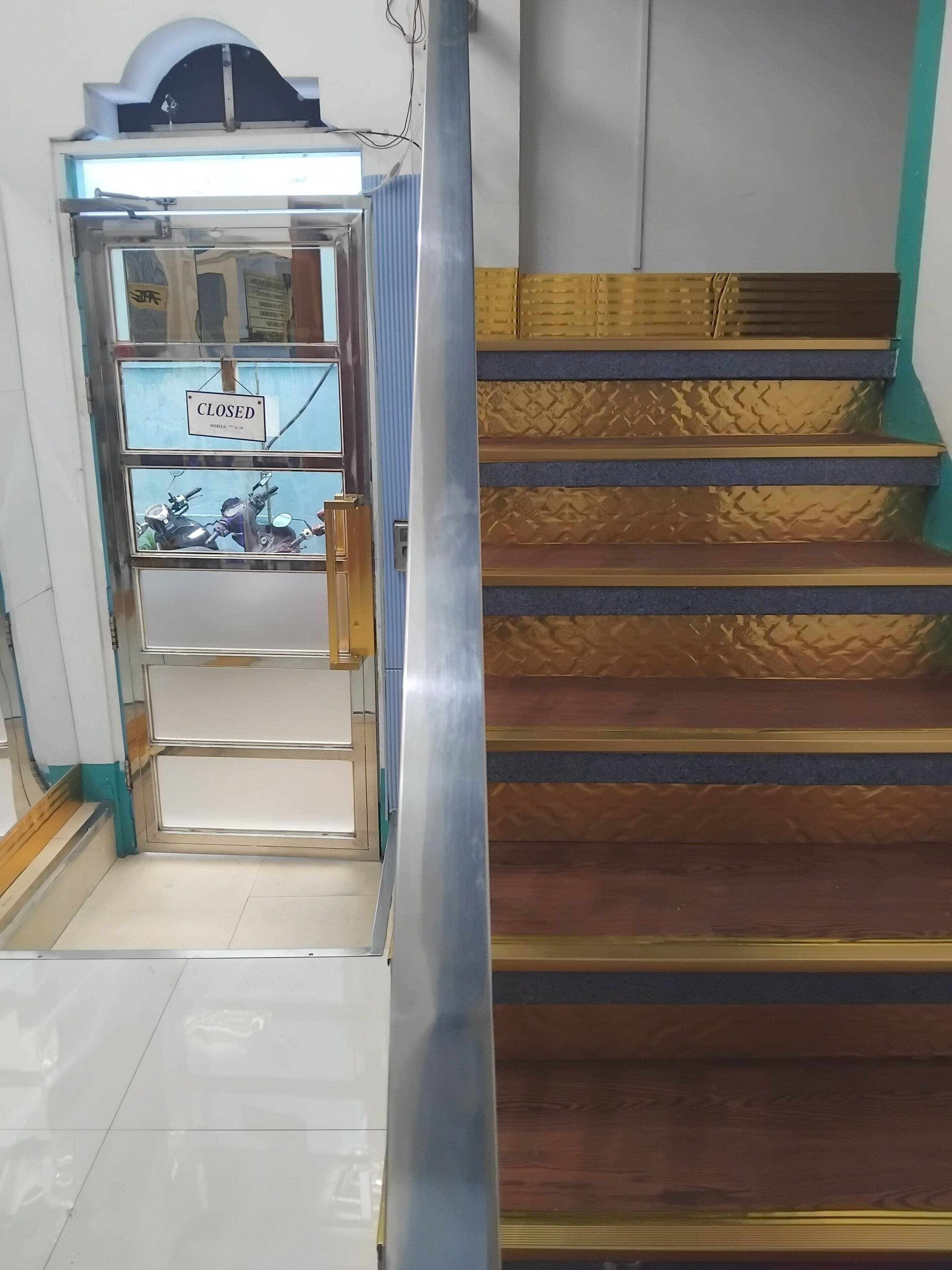 Une entrée fermée avec une pancarte, un escalier aux marches décorées et un sol carrelé.