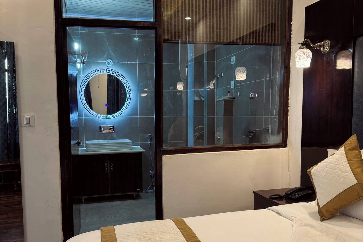 A hotel room with a bed, a vanity with a mirror, a nightstand, and a window with blinds.