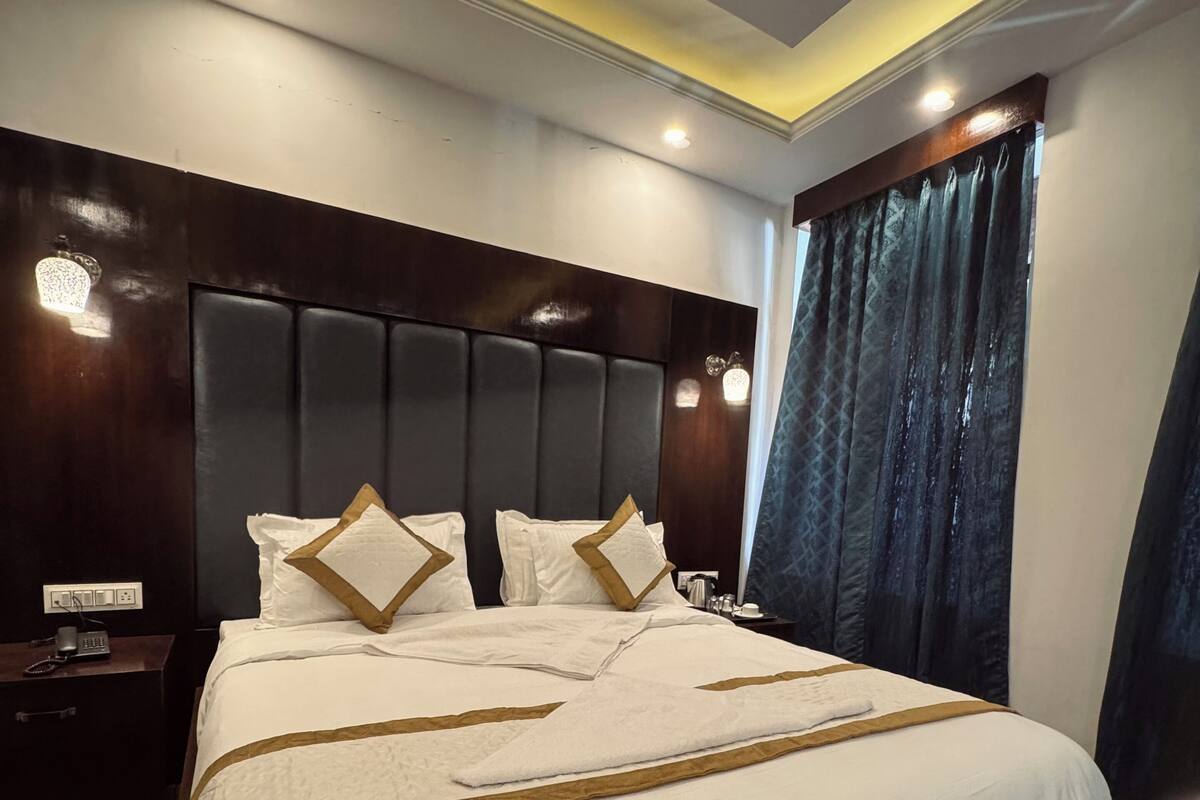 A neatly made bed with a headboard, a bedside table with a lamp, and a window with curtains.