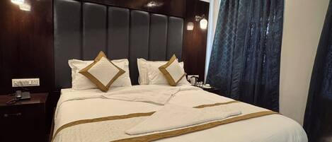 A neatly made bed with a headboard, a bedside table with a lamp, and a window with curtains.