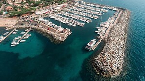 Eine Vogelperspektive auf eine Marina mit zahlreichen vertäuten Booten, umgeben von einem Felssteg und Wohnhäusern im Hintergrund.
