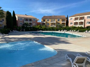 Une piscine entourée de bùtiments à plusieurs étages dotés de balcons, avec des chaises longues à proximité.