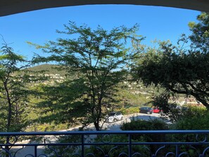 Un balcon avec vue sur une colline, des arbres et une route oĂč circulent des voitures.