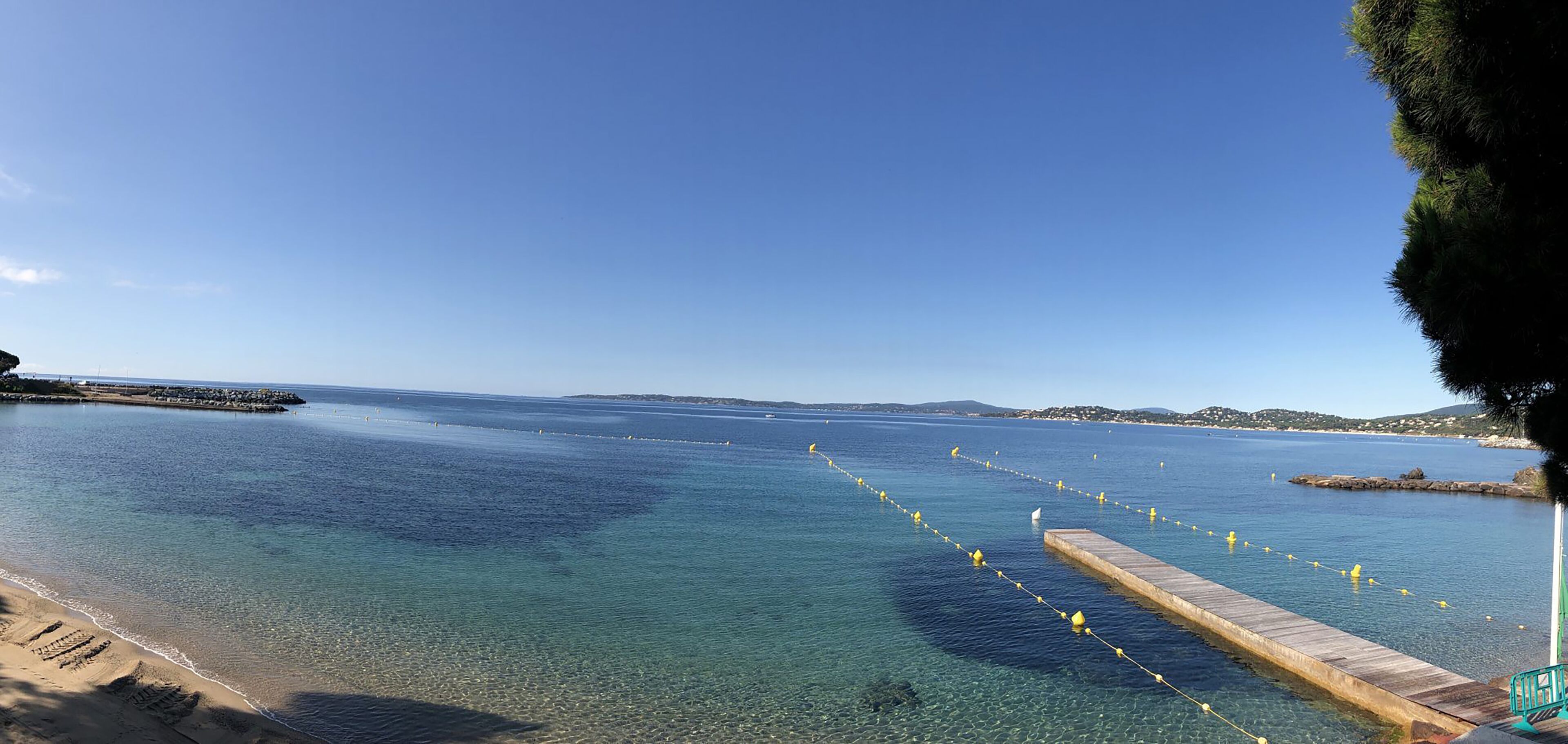 Paisaje costero con agua cristalina, un muelle de madera y una costa distante.