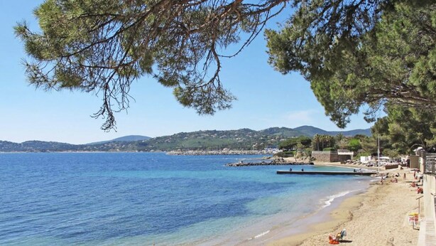Ein Strand mit klarem, blauem Wasser, sandigem Ufer und wenigen Personen.