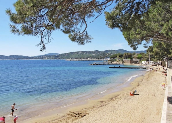 Une plage Ă lâeau claire, bordĂ©e dâun rivage sablonneux, avec des collines en arriĂšre-plan.