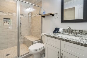 Un baño moderno con ducha envuelta en vidrio, inodoro blanco, lavamanos con encimera de granito y espejo sobre el lavamanos.