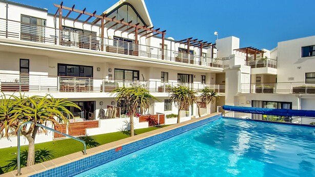 Ein modernes Hotel mit Schwimmbad, mehreren Balkonen und blauem Himmel.