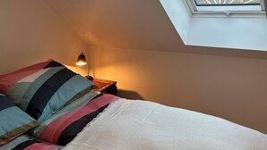 Una camera da letto con un lucernario, un letto con lenzuola a righe e un comodino con una lampada.