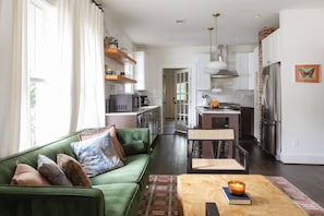 Ein modernes Wohnzimmer mit einem grünen Sofa, einem Couchtisch mit einer Kerze und einer Küche im Hintergrund.