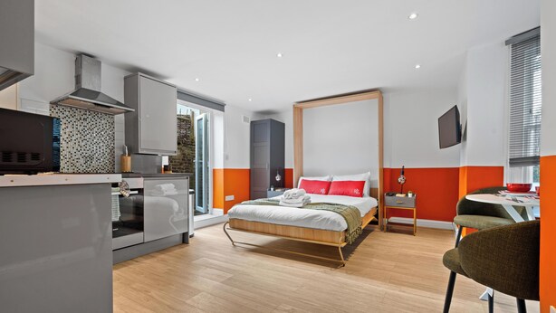 Una habitación de hotel moderna con cama, escritorio, televisor y kitchenette.