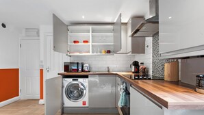 Cocina compacta con lavadora, microondas y encimera de madera.