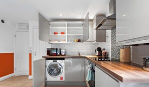 A compact kitchen with a washing machine, microwave, and a wooden countertop. - Boutique Studio - Near Kensington & Notting Hill (London)