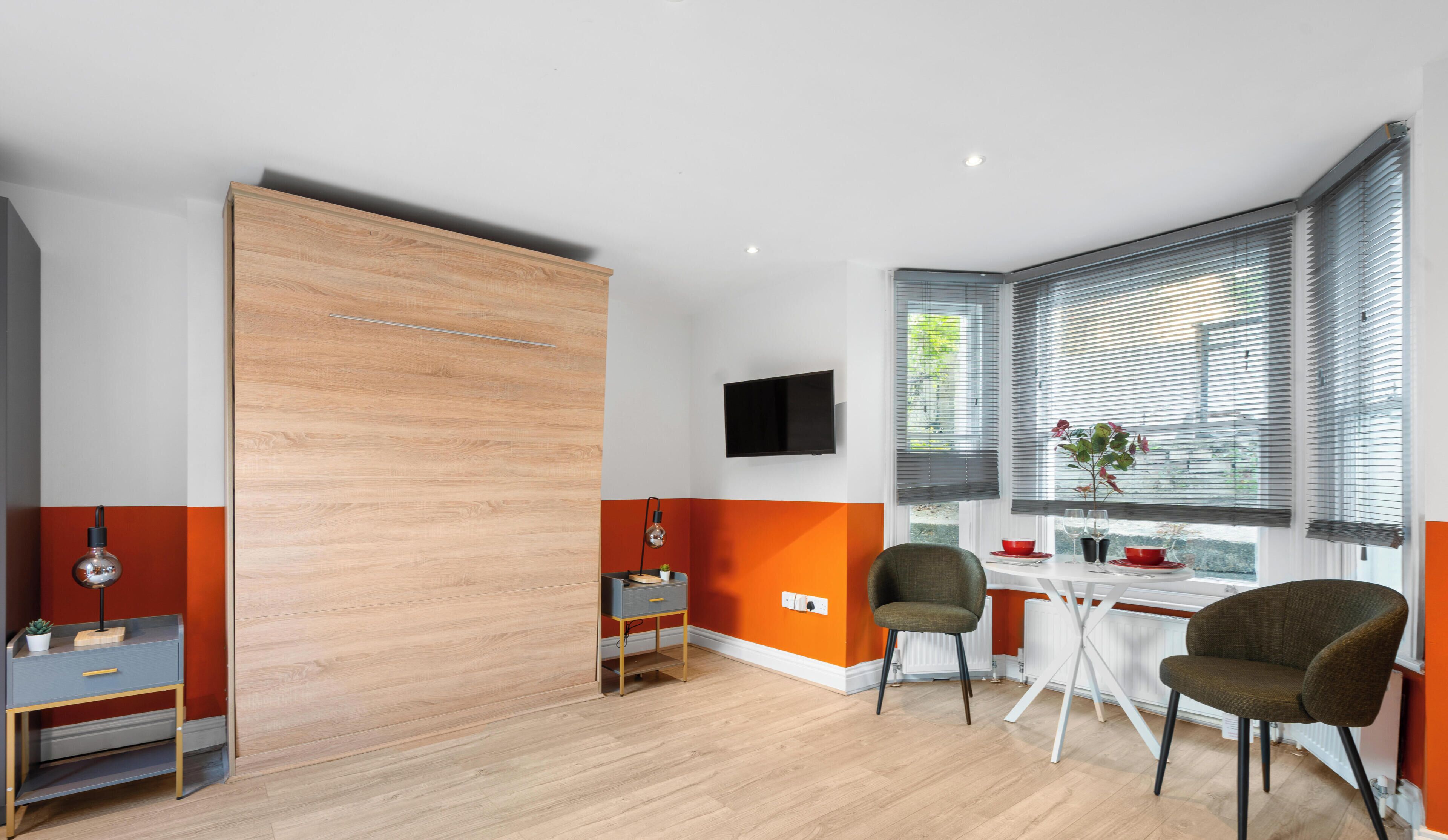 Una habitación moderna con una puerta corredera de madera, un televisor montado en la pared, una mesa de comedor con sillas y una ventana con persianas.