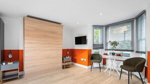 Una habitación moderna con una puerta corredera de madera, un televisor montado en la pared, una mesa de comedor con sillas y una ventana con persianas.