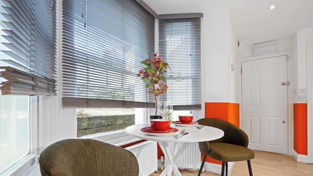 Comedor con mesa redonda, dos sillas, planta en maceta y ventana con persianas.