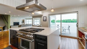 A modern kitchen with a central island, stainless steel appliances, and a sliding glass door leading to an outdoor deck. - Hull Bay Waterfront Home: Private Dock & Apartment (Hull)
