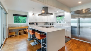 A modern kitchen with a large island, bar stools, stainless steel appliances, and a view of greenery outside. - Hull Bay Waterfront Home: Private Dock & Apartment (Hull)