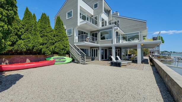 A modern multi-story house with a covered outdoor area, a staircase leading to a balcony, and a view of the water. - Hull Bay Waterfront Home: Private Dock & Apartment (Hull)